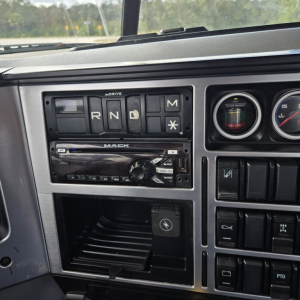 Dashboard cockpit of a 2019 Mack truck showing gear selector panel with R N D M indicators and Mack branded radio, gauges, and switch panel.