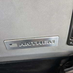 Anthem logo plate on dashboard of a 2019 Mack Anthem day cab truck showing metallic Anthem badge.