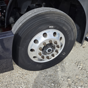 Truck wheel showing a silver steel rim with multiple lug nuts and a large tire mounted on a Mack ANTHEN day cab truck.