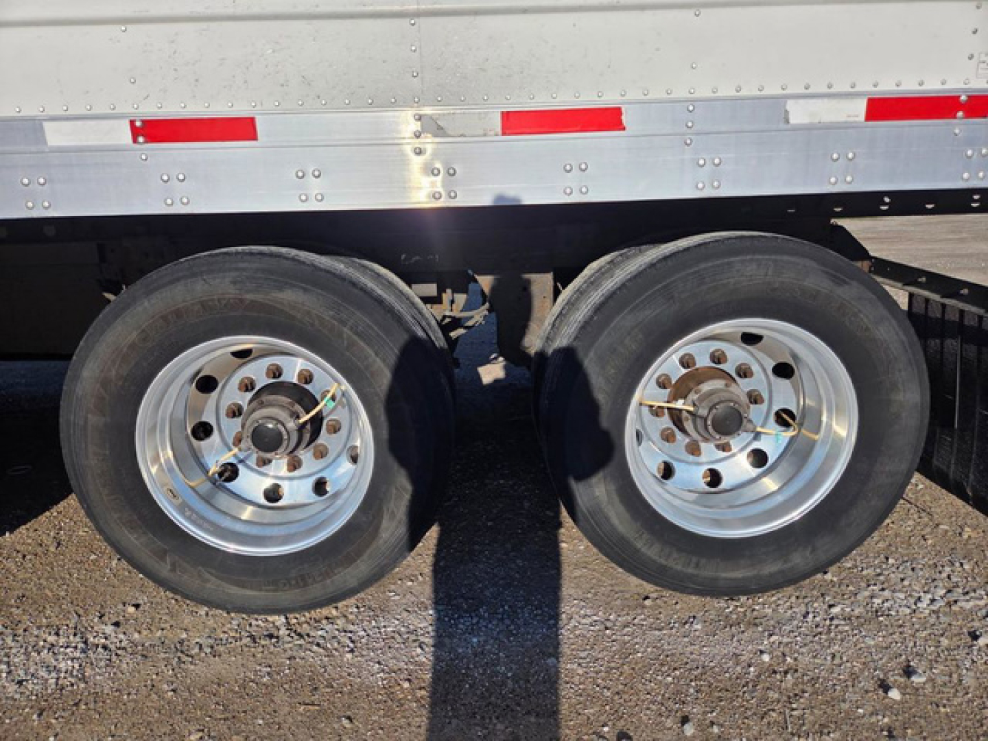 Trailer dual rear axles with wheels and silver aluminum fender; side of refrigerated trailer with riveted metal and red/white reflective tape.