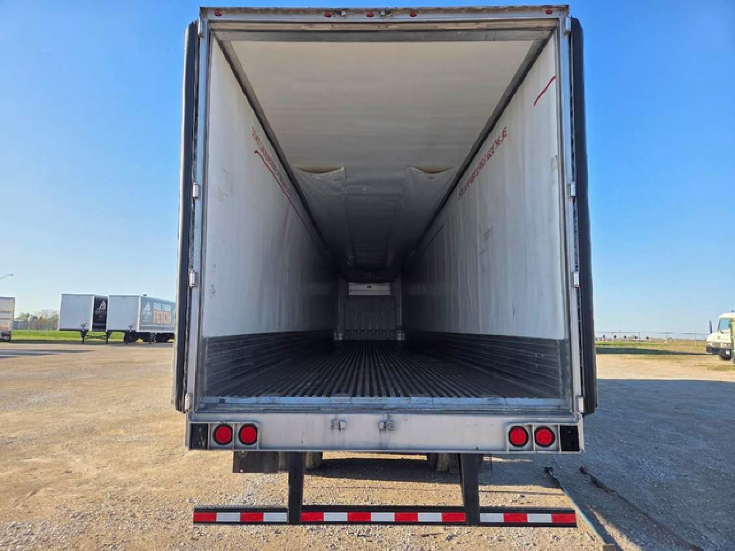 Rear view of a refrigerated trailer open cargo area, empty interior with white walls and ribbed floor, taillights and bumper visible.