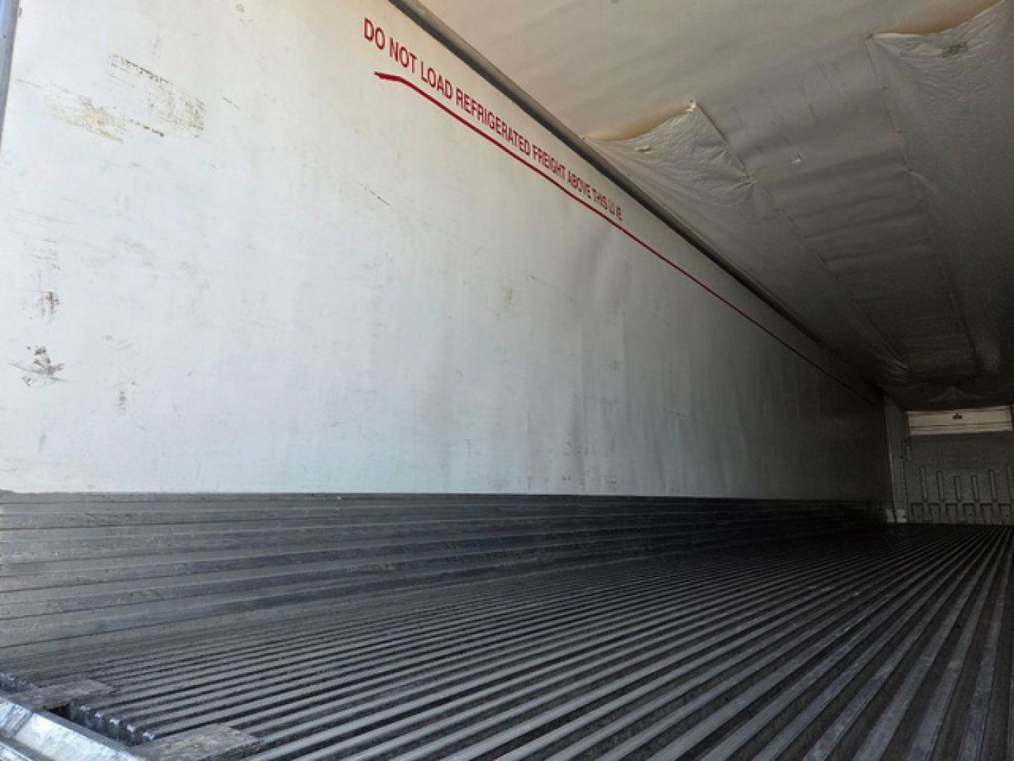 Utility reefer trailer interior with white side walls and ribbed floor, red warning text 'DO NOT LOAD REFRIGERATED FROZEN...' along the top, cargo area empty.