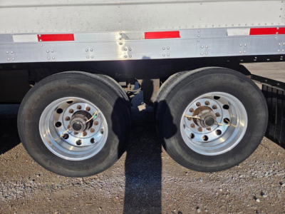 Trailer dual rear axles with wheels and silver aluminum fender; side of refrigerated trailer with riveted metal and red/white reflective tape.