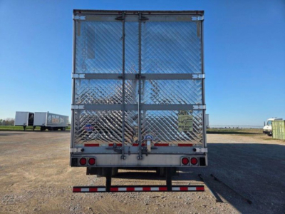 Trailer rear view showing diamond-plate aluminum doors, rear lights, bumper, and locking mechanism on a refrigerated container; clear sky and other trailers in background.