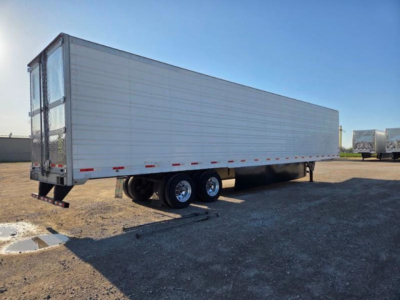 Utility refrigerated trailer in trailer yard showing tandem rear wheels and smooth white-sided box with doors at the front and rear.