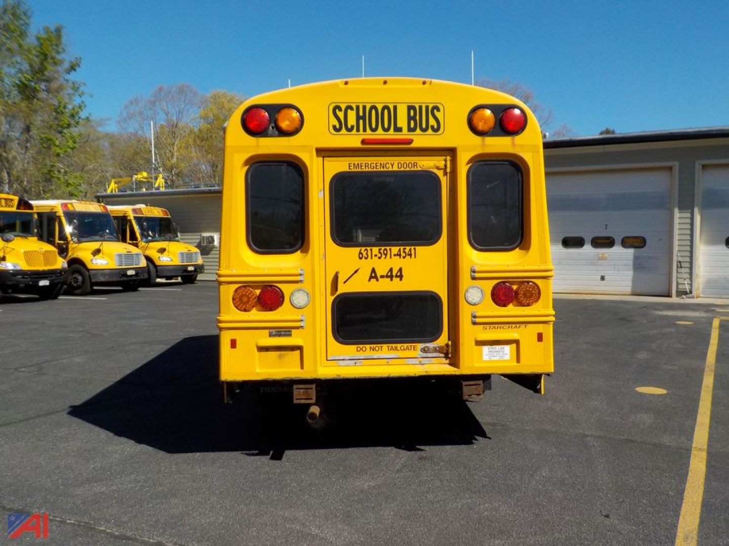 Rear view of a yellow school bus with 'SCHOOL BUS' sign, emergency door, and small text labels visible on the back.
