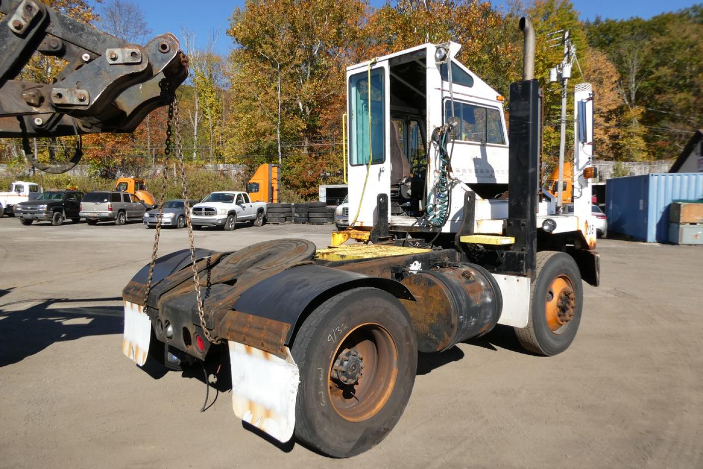 Rear view of a heavy-duty truck tractor with a white cab and orange wheels, showing hitch and rear fenders; part of an excavator arm visible on left.