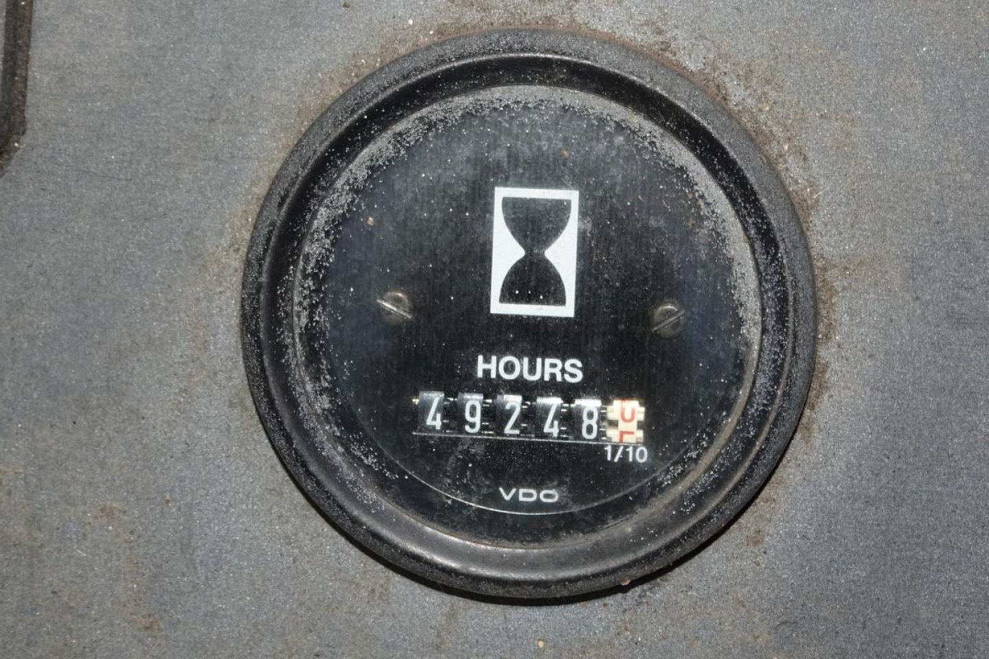 Dial gauge showing hours with an hourglass icon and the numbers 492748? or 4927 8? The label VDO at bottom; surrounding metal surface with dirt.