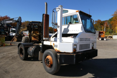 Equipment tractor with white cab and black base in yard showing exhaust stack and rear hitch.
