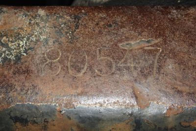 Rusted metal surface with faded handwritten numbers 80547 and rough texture.