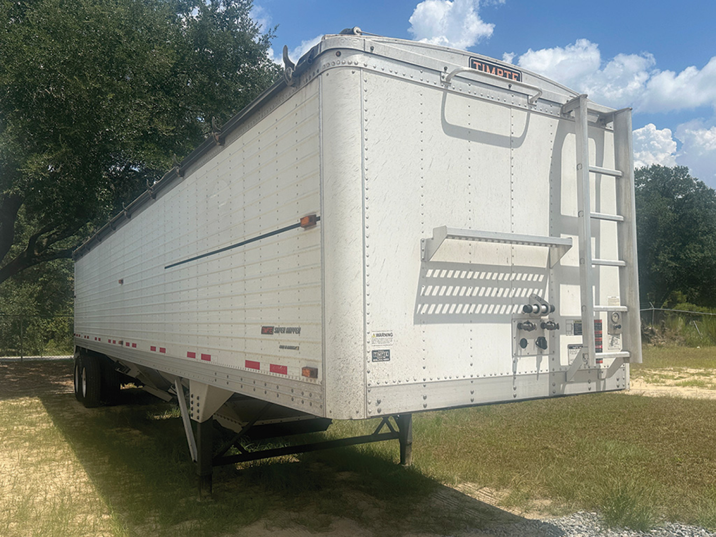 Timpte Super Hopper trailer rear-left angle showing ladder, rear doors, and underside support legs with reflective tape.