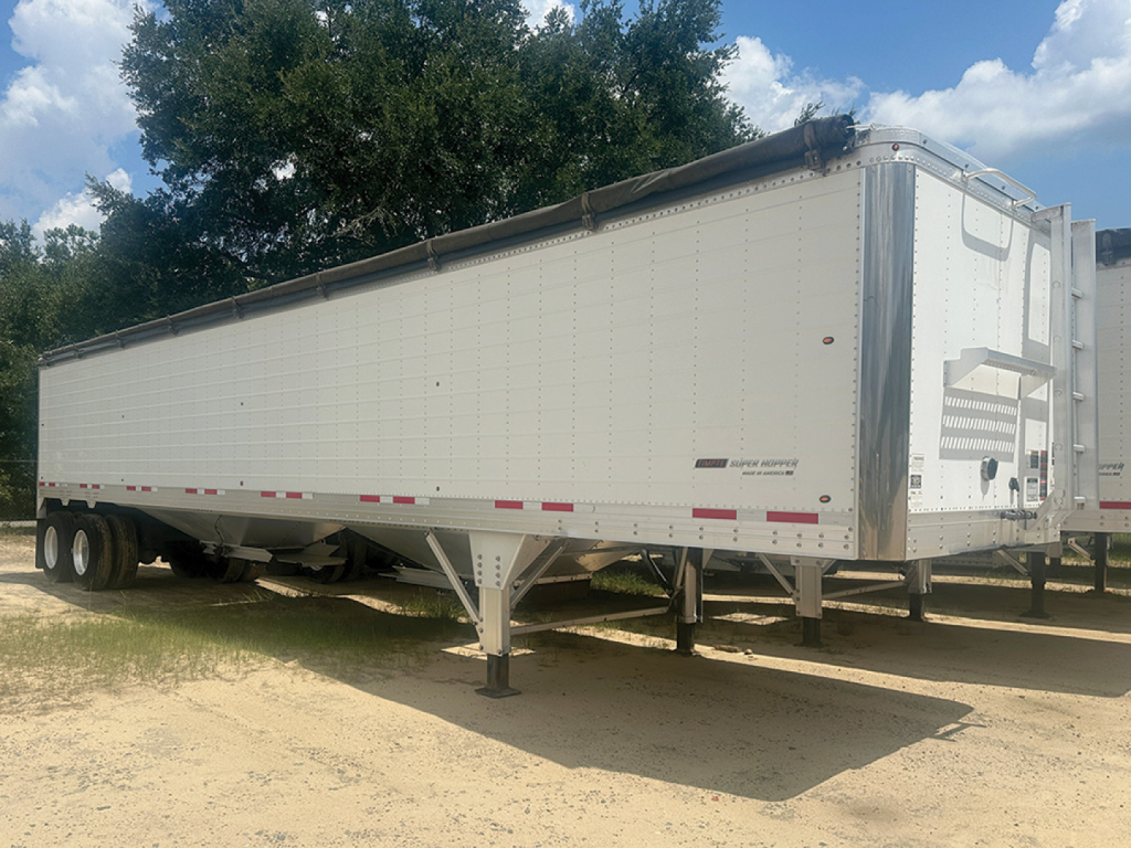 Timpte Super Hopper trailer side view showing aluminum hopper with landing legs and reflective tape. Nozzled text near rear with brand markings and model details not legible.