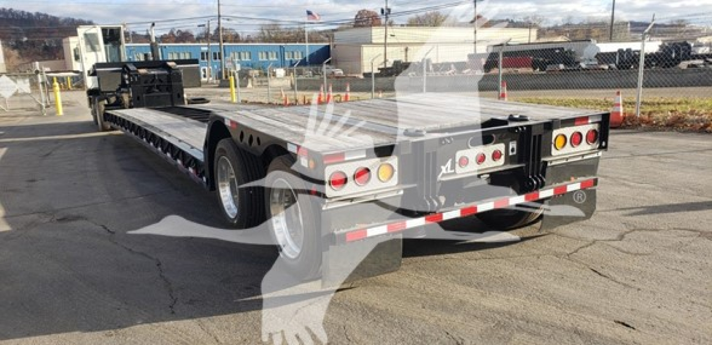 Flatbed trailer in a yard showing long multi-axle 80HDG specialized trailer with rear lights and reflective tape.