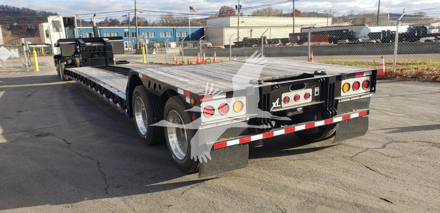 Lowboy trailer showing dual rear axles and flatbed deck with reflective striping and rear light cluster.