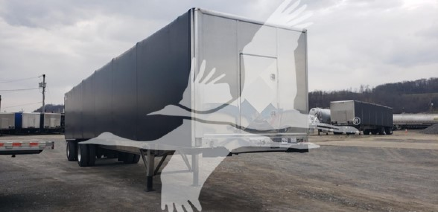 Trailer in a lot: Benson aluminum flatbed Curtainside trailer showing long rectangular cargo area and rear access door.