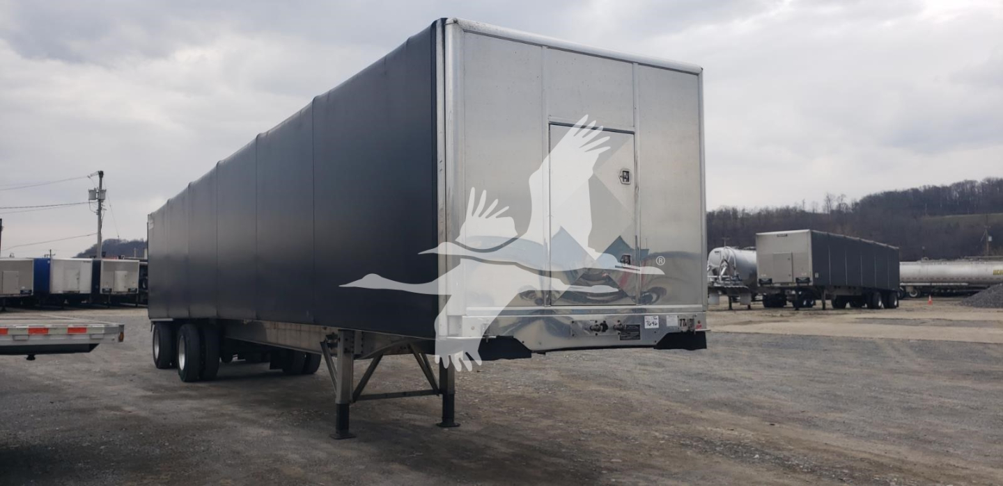 Trailer side view showing a Benson flatbed curtainside trailer with grey panels and rear doors in a truck yard.