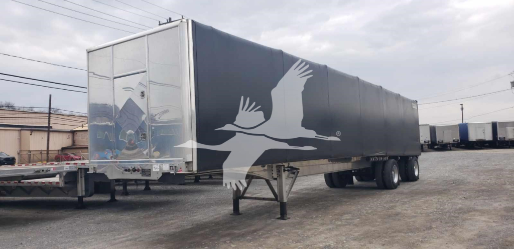 Trailer in yard showing Benson curtainside flatbed with graphic white birds on dark tarp and rear doors.