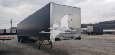 Trailer side view showing a Benson flatbed curtainside trailer with grey panels and rear doors in a truck yard.