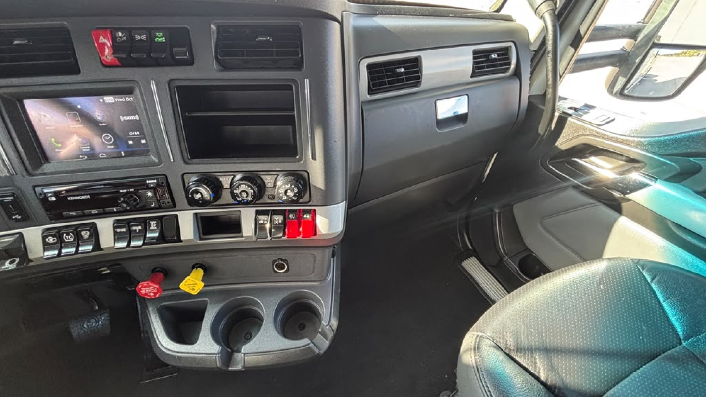 Kenworth T680 cab interior showing center console with controls, touchscreen display, gear levers, cup holders, and dashboard accents.