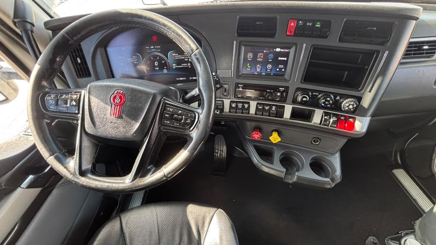 Kenworth T680 dashboard and steering wheel with digital display, control buttons, and cup holders in view.