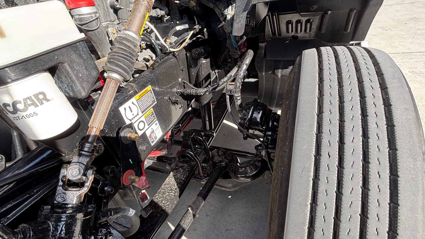 Kenworth T680 engine bay area showing front suspension and wiring with stickered components and a large tire.