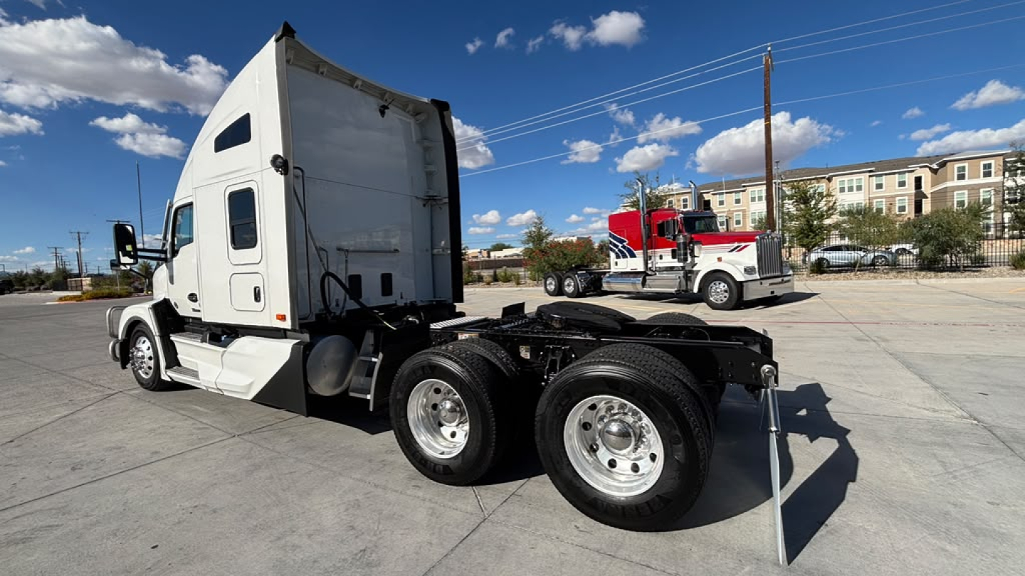 Kenworth T680 tractor in a parking lot, side view showing sleeper cab, rear dual axles, and fifth wheel hitch with no visible branding on side