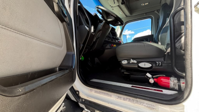 Front cabin entry of a Kenworth T680 truck showing the driver seat, dashboard, and interior panels. Visible text may include control labels and small badges near the door.