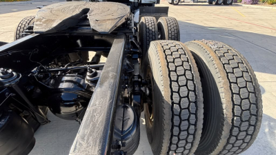 Kenworth T680 chassis with dual rear wheels showing engine bay components and suspension. Visible are truck frame rails, air tanks, and drivetrain near the cab area.