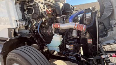 Kenworth T680 engine bay showing coolant reservoir, hoses, and engine components in side view.