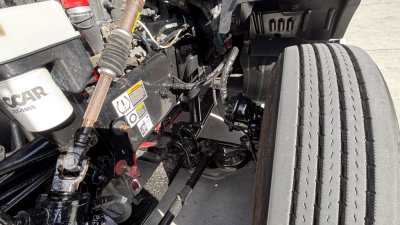 Kenworth T680 engine bay area showing front suspension and wiring with stickered components and a large tire.