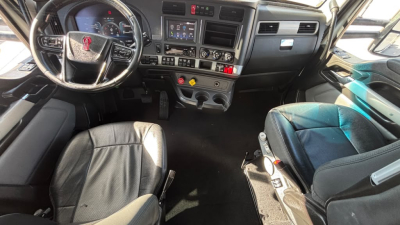 Kenworth T680 truck interior showing steering wheel, driver and passenger seats, dashboard with screens and controls.