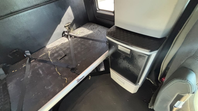 Kenworth T680 interior sleeper cab area with driver seat and overhead storage, showing a metal platform and seat belt anchors.