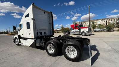 Kenworth T680 tractor in a parking lot, side view showing sleeper cab, rear dual axles, and fifth wheel hitch with no visible branding on side