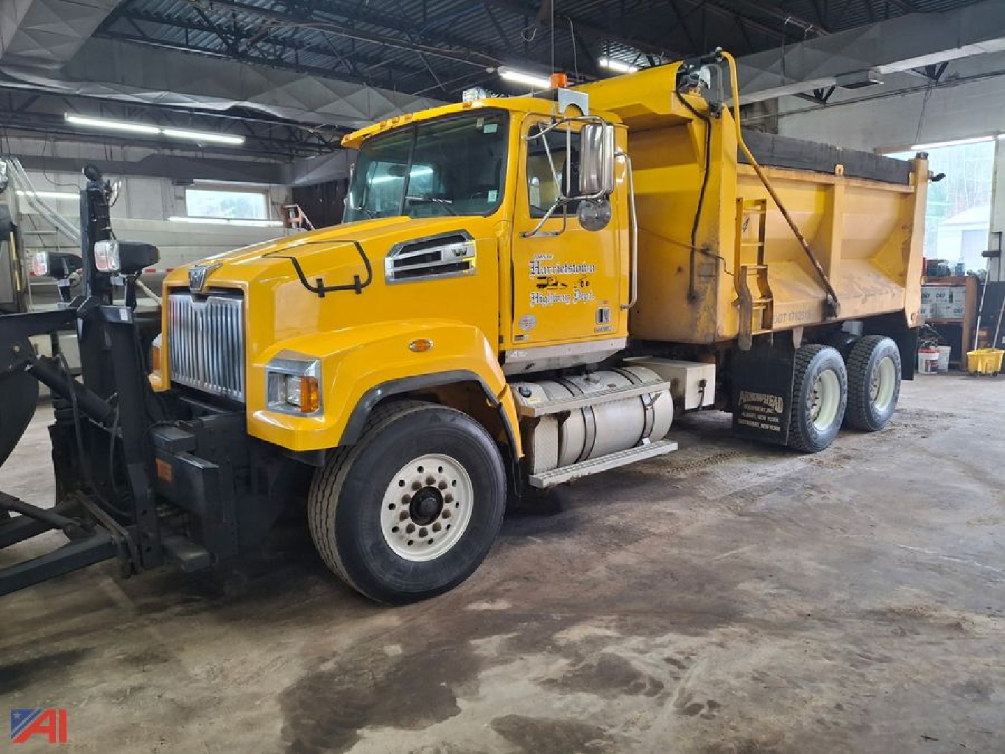 Yellow Western Star 4700 dump truck inside a garage, side view showing the front grille, cab, and large dump bed.