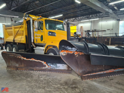 Yellow Western Star 4700 dump truck in a warehouse with large snow plow blades in front, side view of cab and bed.
