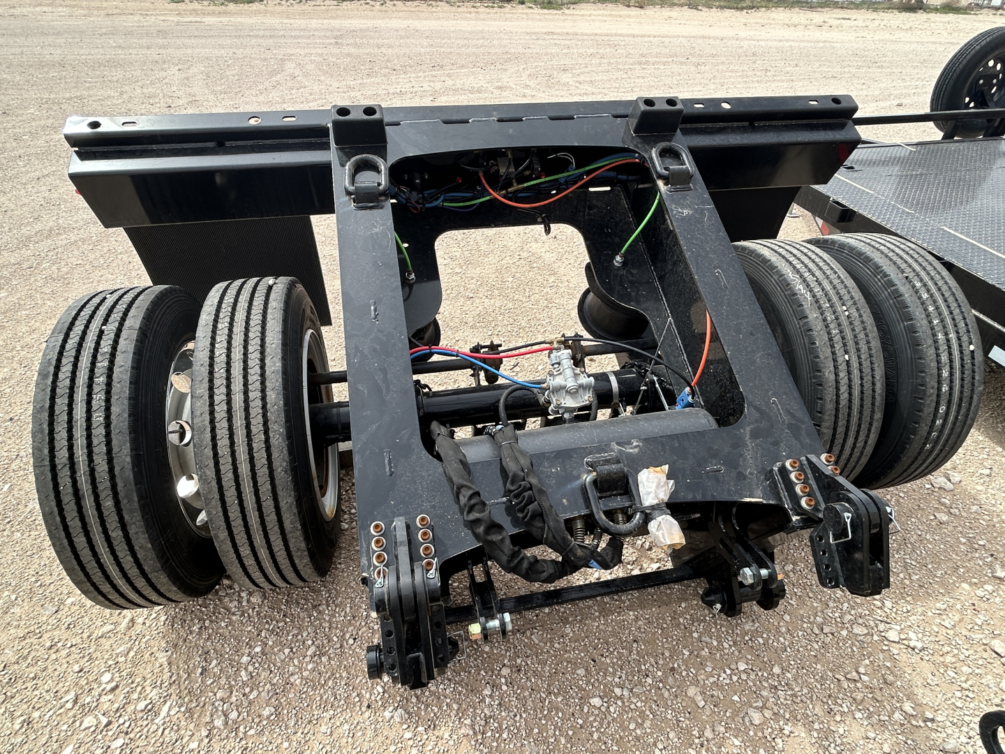 Load King flip axle trailer subframe showing dual rear axles and wiring harness with hydraulic components and connectors visible.