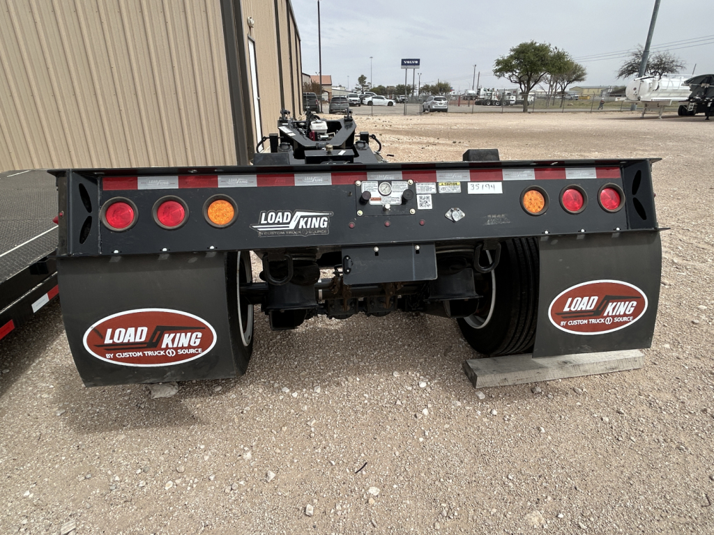 Load King trailer rear view showing flip axle with taillights, mud flaps labeled Load King, and stickers. Visible text includes LOAD KING logo and circular decals on mud flaps, and small label near center with VIN/serial-like numbers.