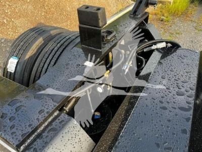 Fontaine Flip Axle trailer component view showing hydraulic hoses and mounting frame with wet surface and spare tire in background.