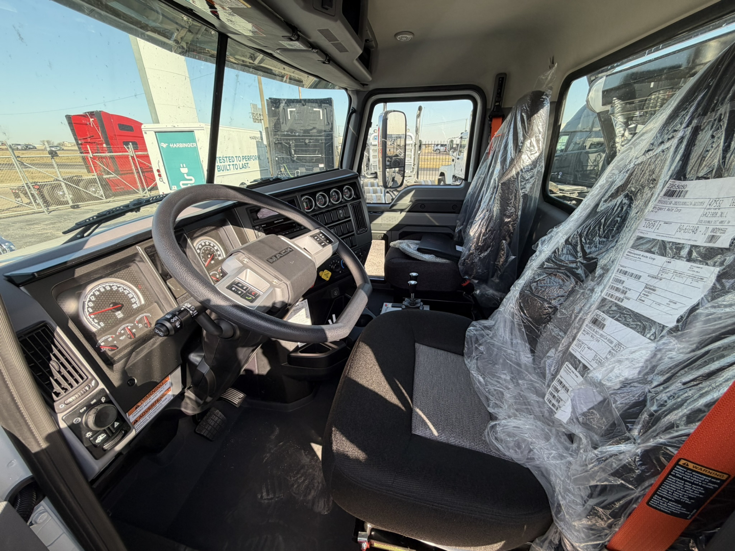 Mack GR64B truck cab interior showing steering wheel, dashboard gauges, and plastic-covered seats