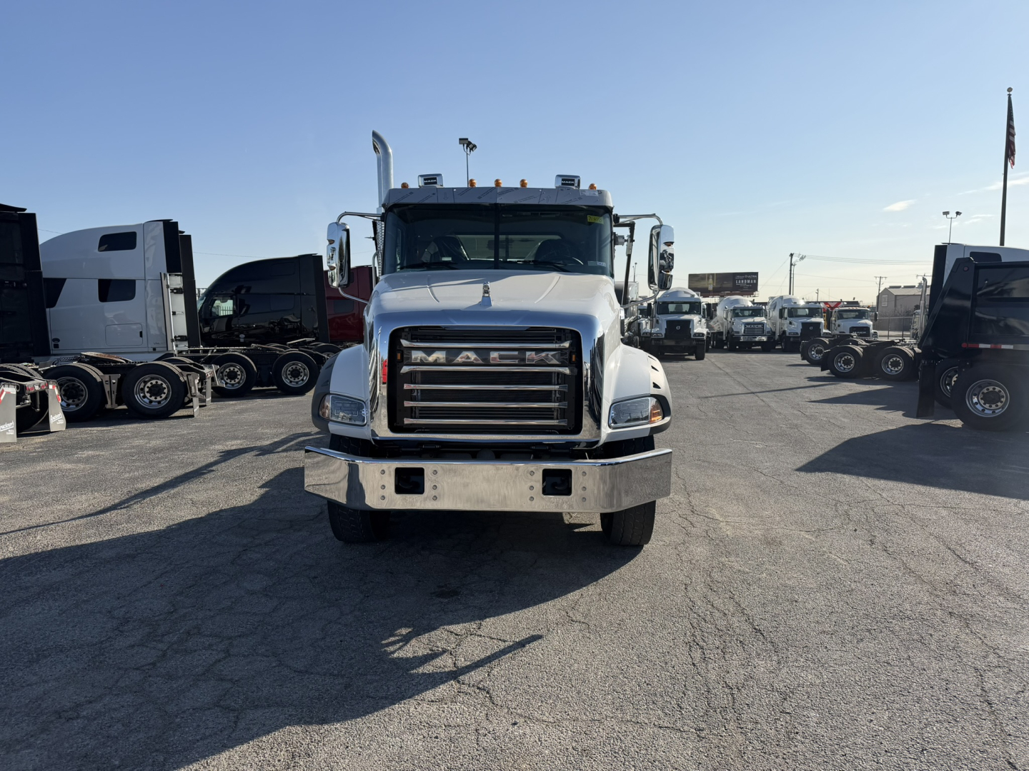Front view of a white 2026 Mack GR64B truck in a dealership lot, grille prominently displayed, multiple trucks in background.