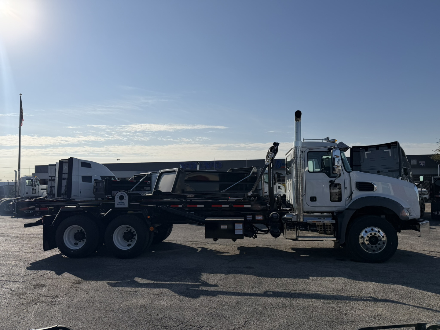 2026 Mack GR64B roll-off truck with flatbed, side view showing dual rear axles and hoist mechanism.