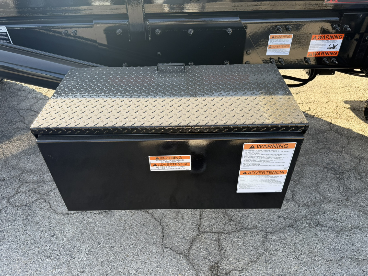 Rolloff truck toolbox mounted on a frame with diamond plate lid and warning labels visible on the side.