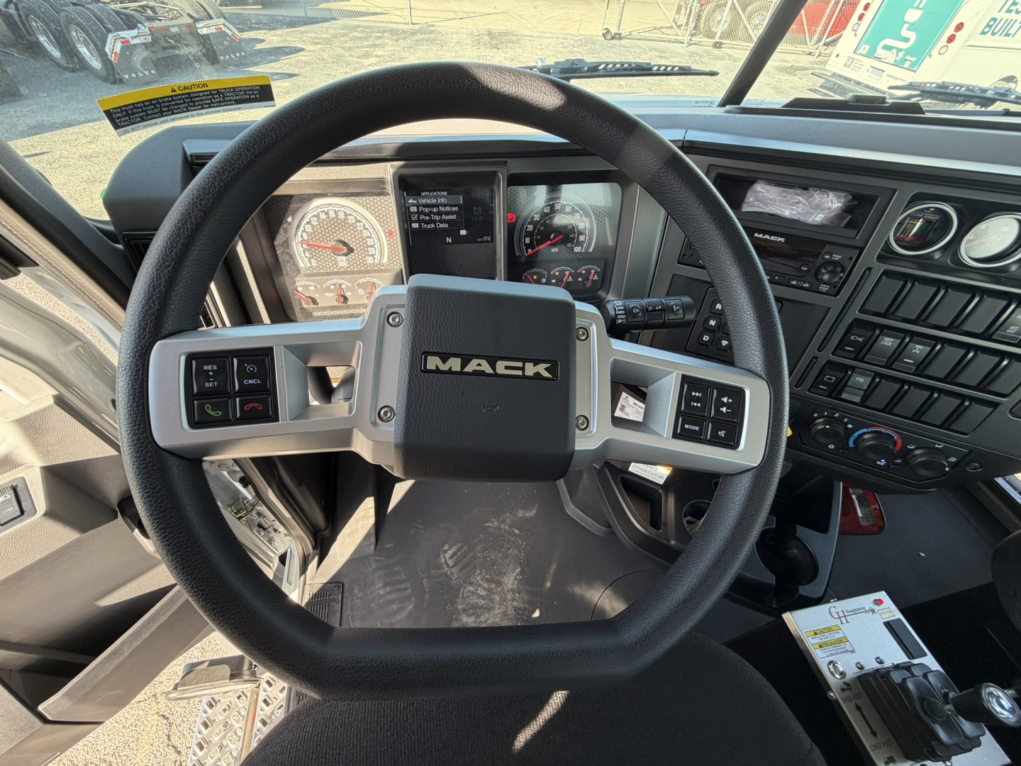 Mack GR64B truck interior steering wheel dashboard with Mack logo center and digital gauges visible.