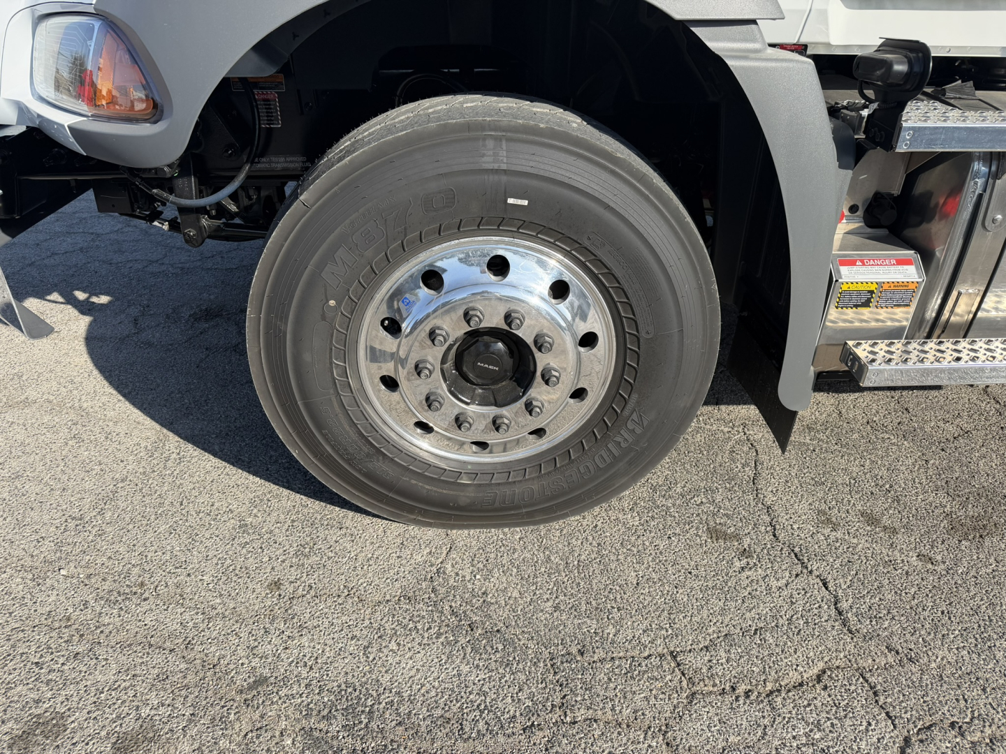 Wheel end of a 2026 Mack GR64B rolloff truck showing front tire and polished steel wheel with hub, surrounding chassis components.