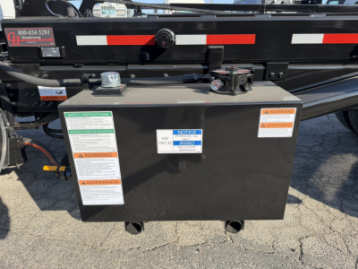 Mack GR64B roll-off truck battery box with multiple warning labels and access caps visible.