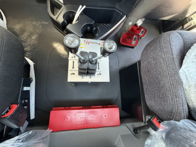 Mack GR64B cab interior showing dual gauges and control panel between seats; clear view of pedals and center console area.