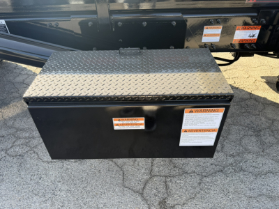 Rolloff truck toolbox mounted on a frame with diamond plate lid and warning labels visible on the side.