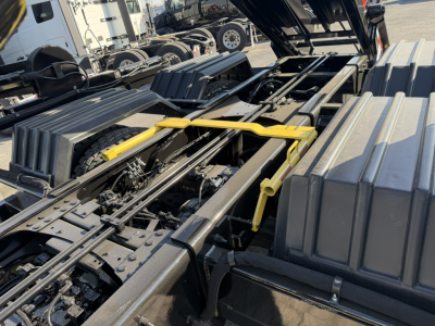 Mack GR64B truck chassis with hydraulic components and cab tilt visible, showing frame rails, hoses, and tool/storage boxes.