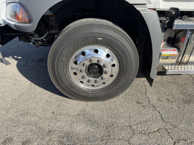Wheel end of a 2026 Mack GR64B rolloff truck showing front tire and polished steel wheel with hub, surrounding chassis components.
