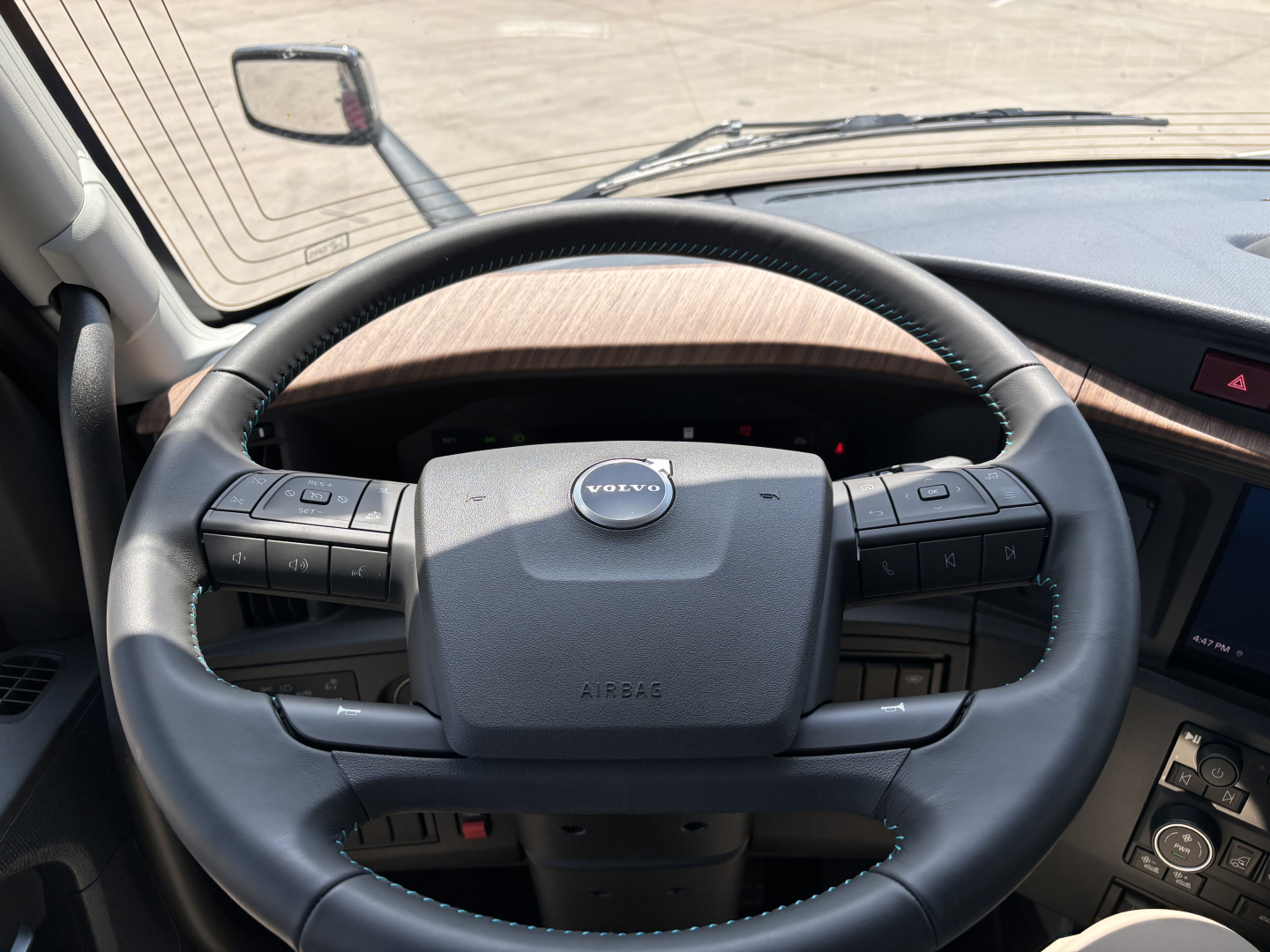 Volvo truck steering wheel in-cab view showing steering wheel with Volvo logo and control buttons.